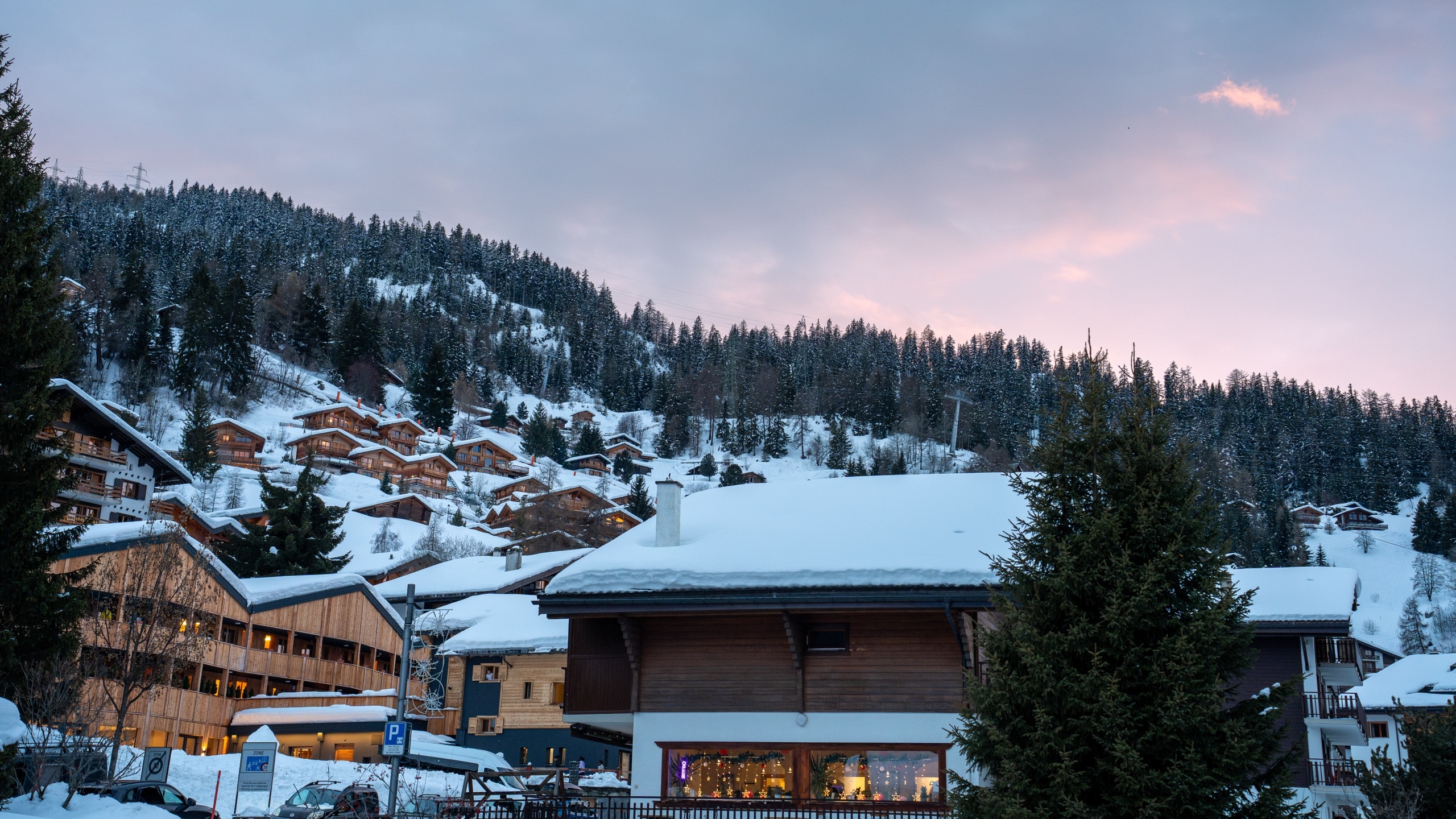 Snow-covered alpine village with wooden chalets at twilight under a pink and blue sky