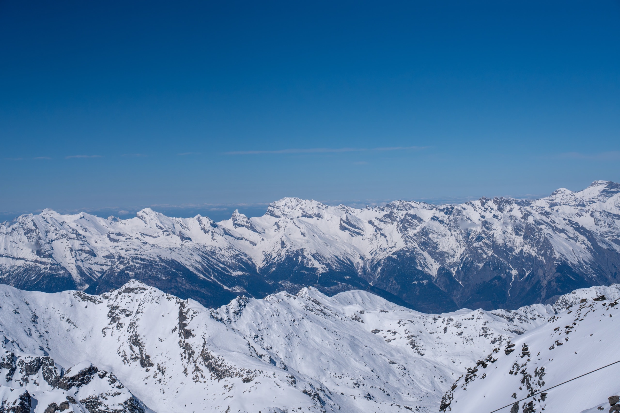 Panoramic view of jagged snow-capped mountain peaks under a clear deep blue sky